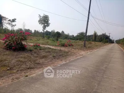 Expansive land plot with potential for development, featuring lush greenery and a paved road access.