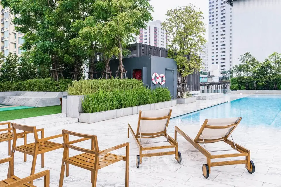 Luxurious outdoor pool area with stylish wooden loungers and lush greenery in a modern residential complex.