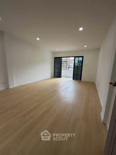 Spacious empty living room with wooden flooring and large windows leading to a balcony.
