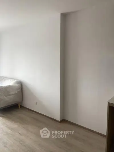 Minimalist bedroom with wooden flooring and simple bed setup.