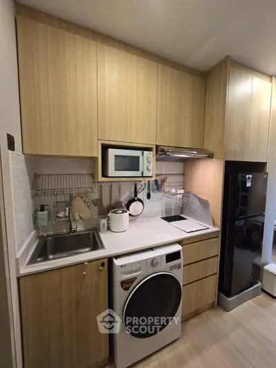 Modern compact kitchen with wooden cabinets, washing machine, microwave, and fridge, perfect for urban living.