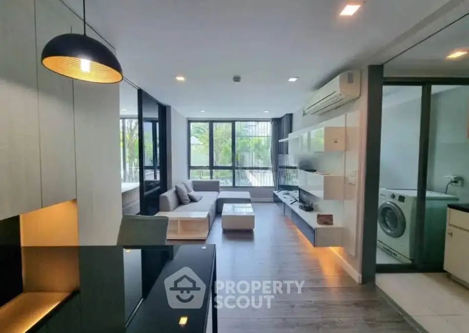 Modern living room with open layout and stylish decor, featuring large windows and a washing machine area.