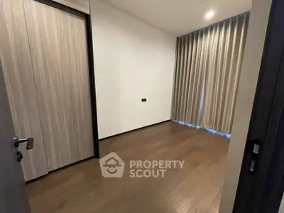 Spacious empty room with wooden flooring and large window curtains, ideal for customization.