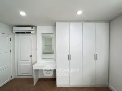 Modern bedroom with white wardrobe and vanity, featuring sleek design and ample storage.
