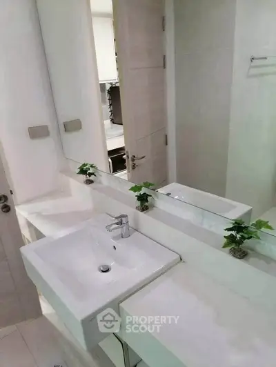 Modern bathroom with sleek white sink and large mirror, minimalistic design.