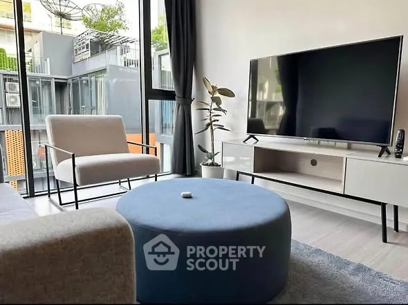 Modern living room with large TV, stylish furniture, and floor-to-ceiling windows offering natural light.