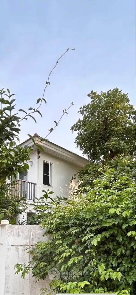 Charming white house with lush greenery and a quaint balcony, perfect for serene living.