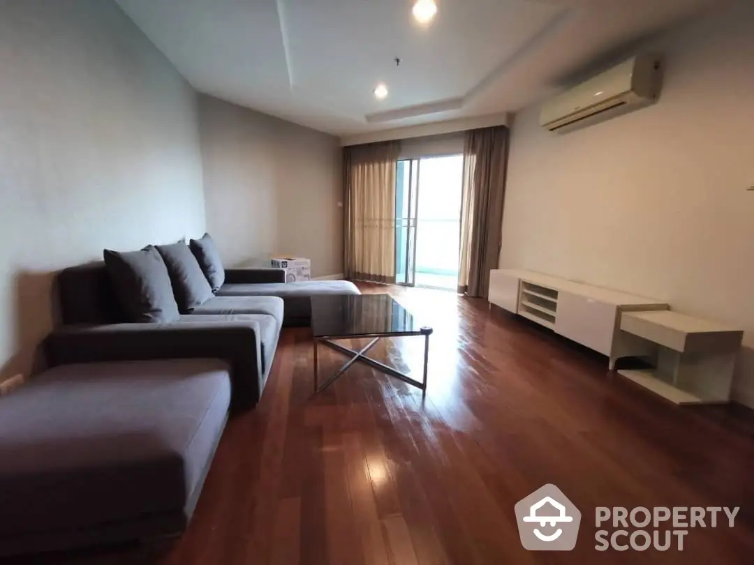 Spacious living room with polished hardwood floors, modern furniture, and ample natural light from large windows, ideal for comfortable urban living.