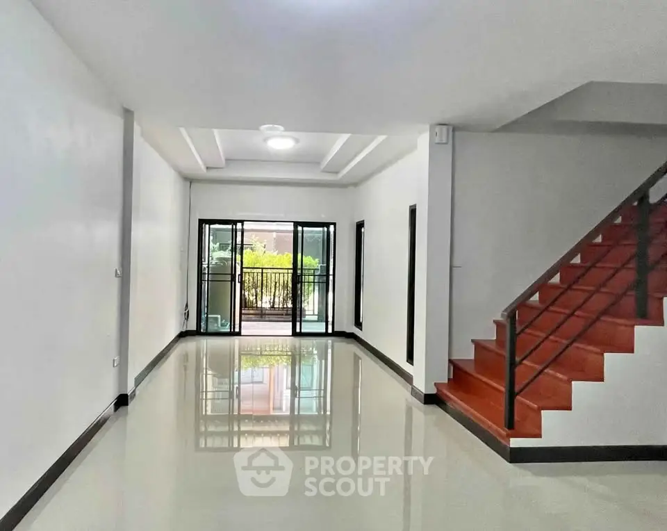 Spacious modern living room with sleek staircase and large windows leading to a balcony.