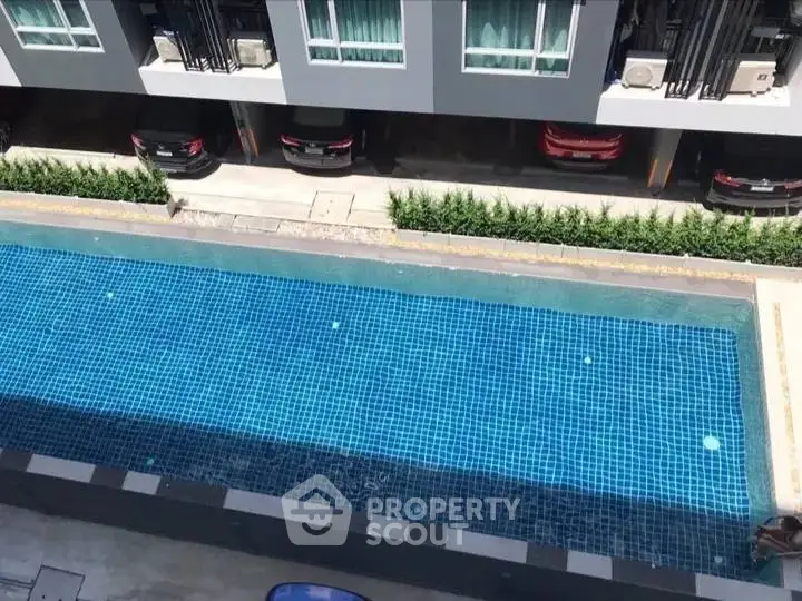 Modern apartment complex with a sleek swimming pool and parked cars.