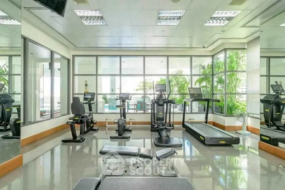 Spacious gym with modern equipment and large windows offering natural light.