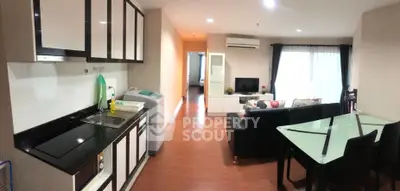 Modern open-layout living room with kitchen and dining area, featuring sleek furniture and bright lighting.