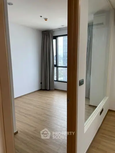 Spacious bedroom with wooden flooring and large window offering city views.