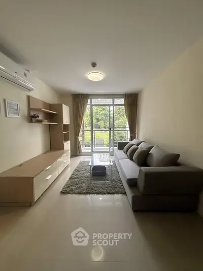 Spacious living room with modern furniture and large window offering natural light and balcony access.