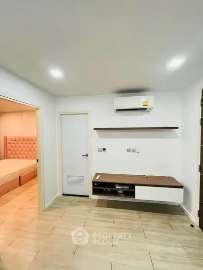 Modern living room with air conditioning and wooden flooring, adjacent to a cozy bedroom.