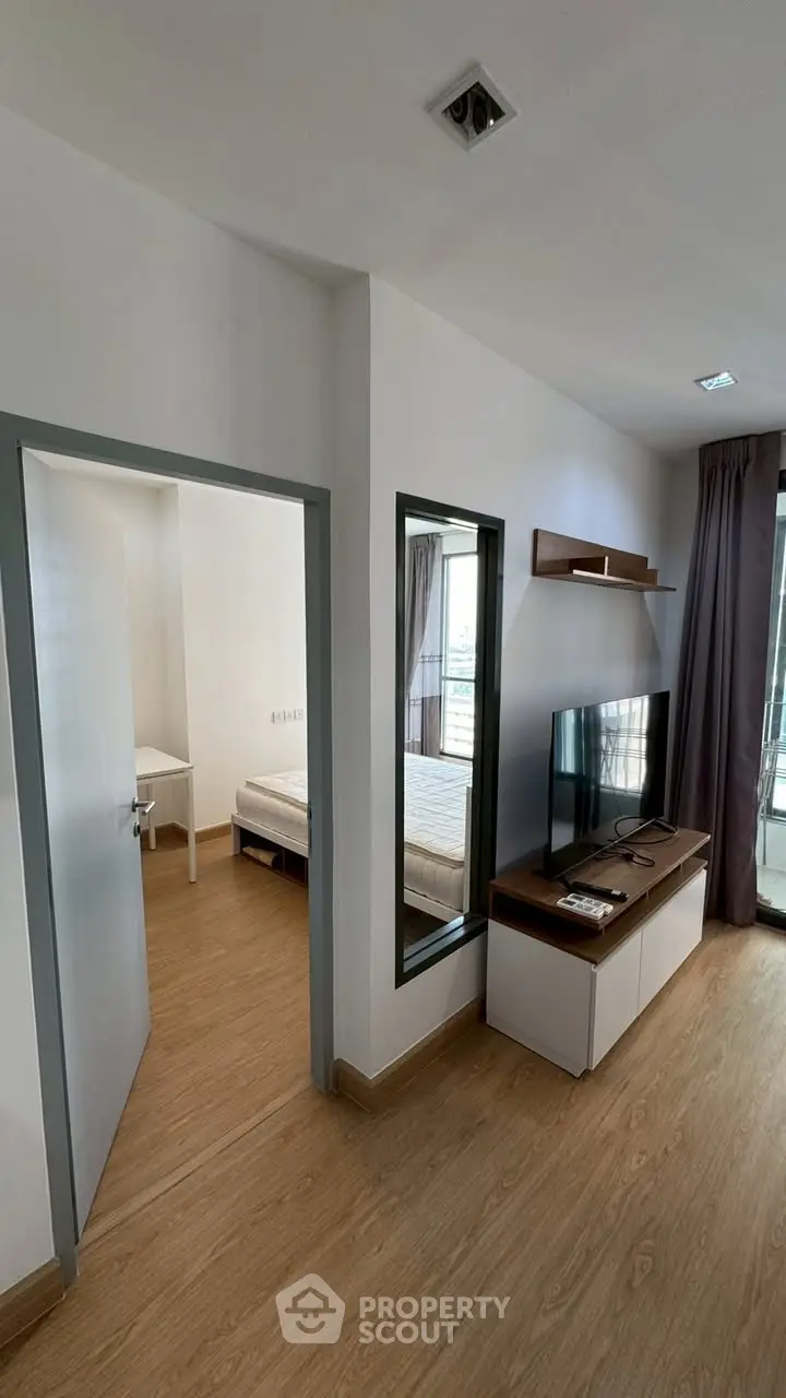 Modern living room with TV and view into bedroom, featuring sleek wooden flooring and contemporary design.