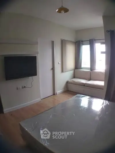 Cozy bedroom with natural light, featuring a wall-mounted TV and a comfortable seating area by the window.