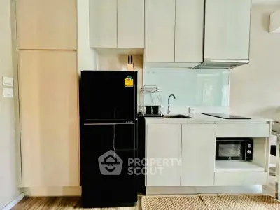 Modern kitchen with sleek cabinetry, black fridge, and built-in microwave in a stylish apartment.