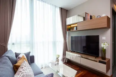 Modern living room with stylish decor and large TV, featuring floor-to-ceiling windows and elegant furnishings.