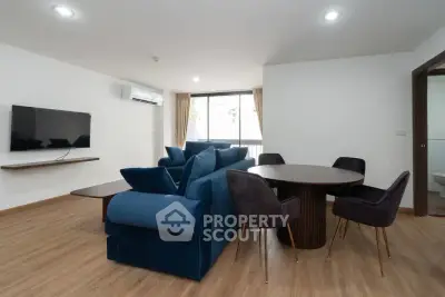 Spacious modern living room with blue sofa and dining area, featuring sleek wooden flooring.
