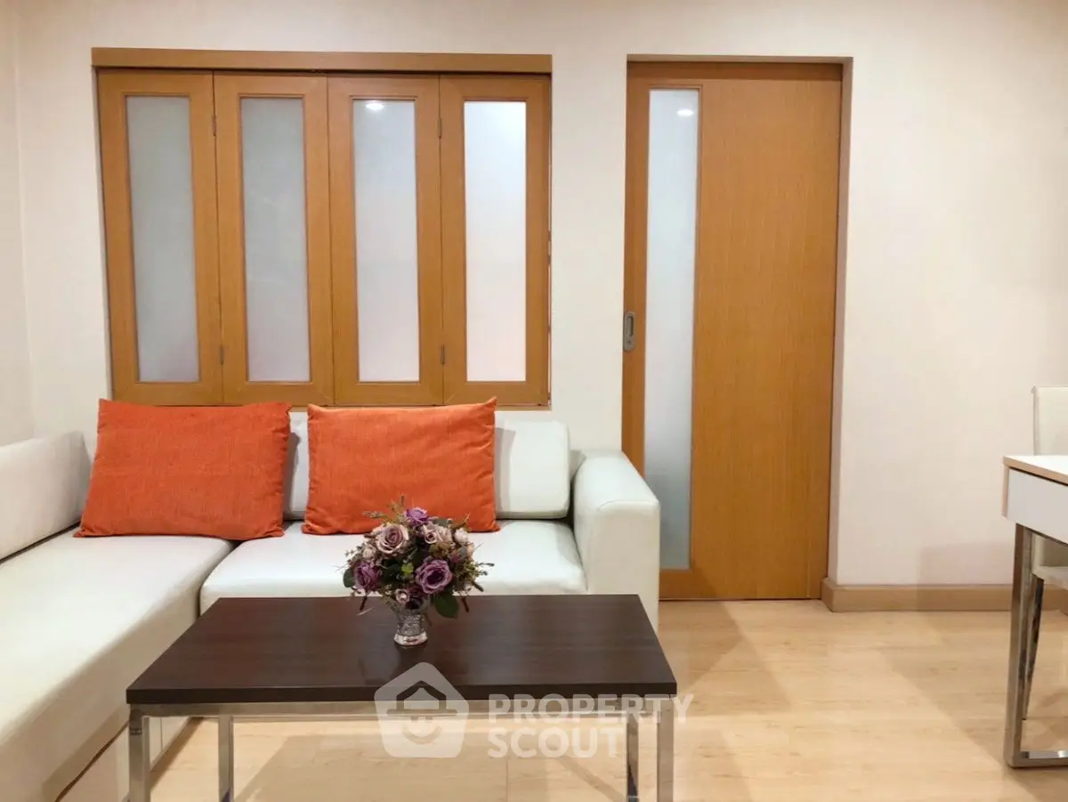 Modern living room with white sofa, orange cushions, and wooden accents.
