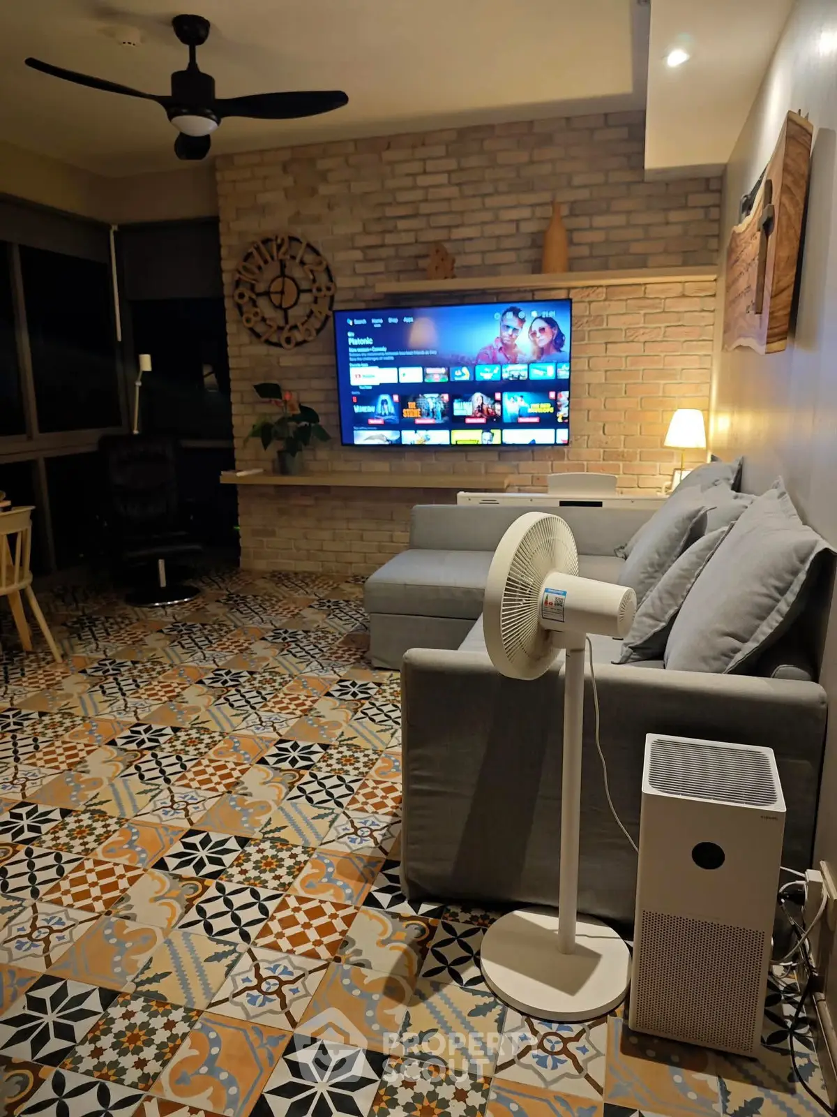 Stylish living room with modern decor and large TV, featuring patterned tile flooring and cozy seating.