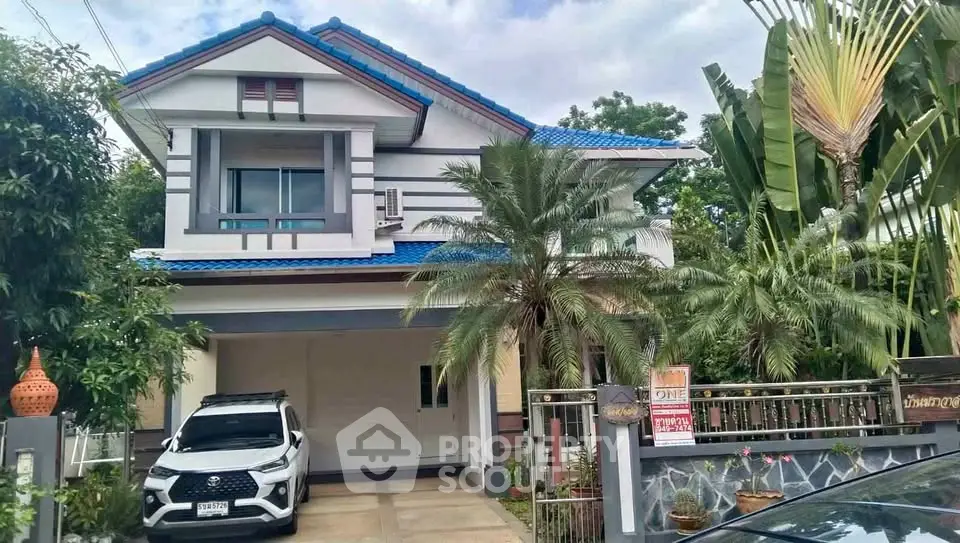 Charming two-story house with blue roof, lush garden, and spacious driveway in a serene neighborhood.