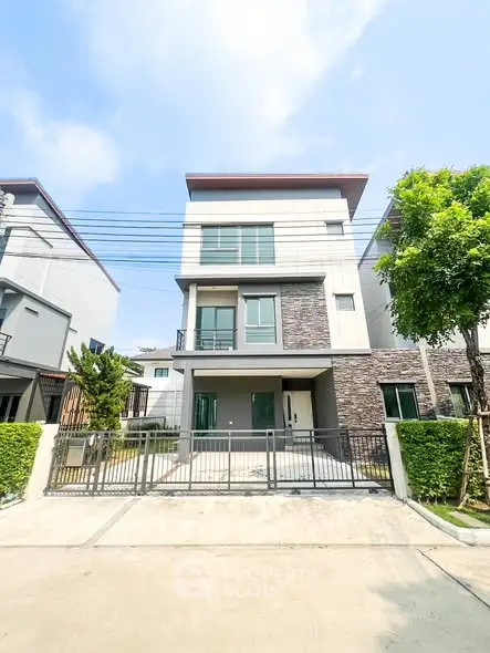 Modern three-story house with sleek design and gated entrance in a suburban neighborhood.