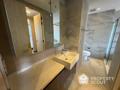 Modern bathroom with sleek marble finishes, large mirror, and glass shower enclosure, offering a luxurious and serene retreat.