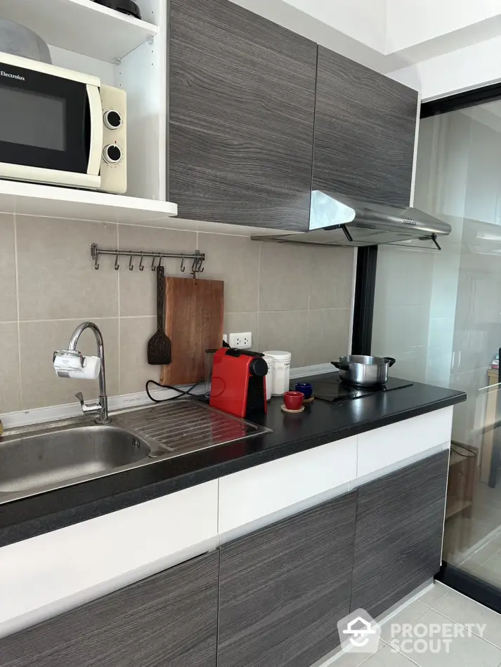 Modern kitchen with sleek cabinetry and appliances, featuring a microwave and coffee maker.