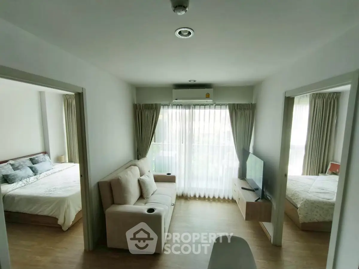 Modern living room with natural light and cozy seating, connecting two bedrooms in a stylish apartment.