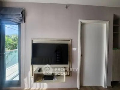 Modern living room with wall-mounted TV and large window offering natural light.