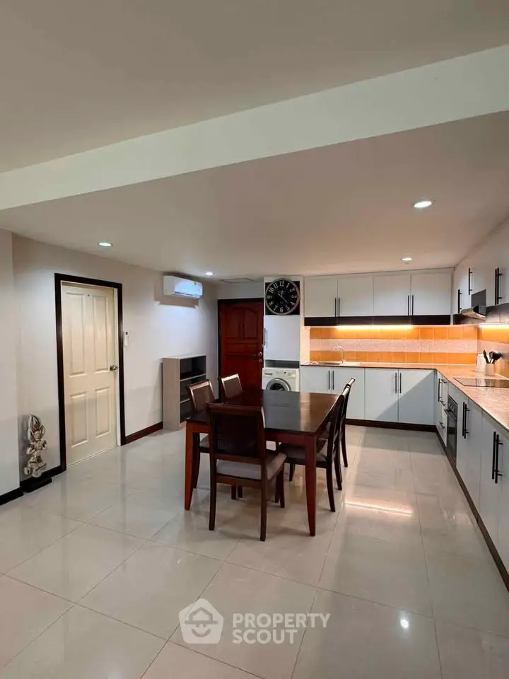 Spacious kitchen with modern cabinetry and dining area, featuring sleek design and ample lighting.