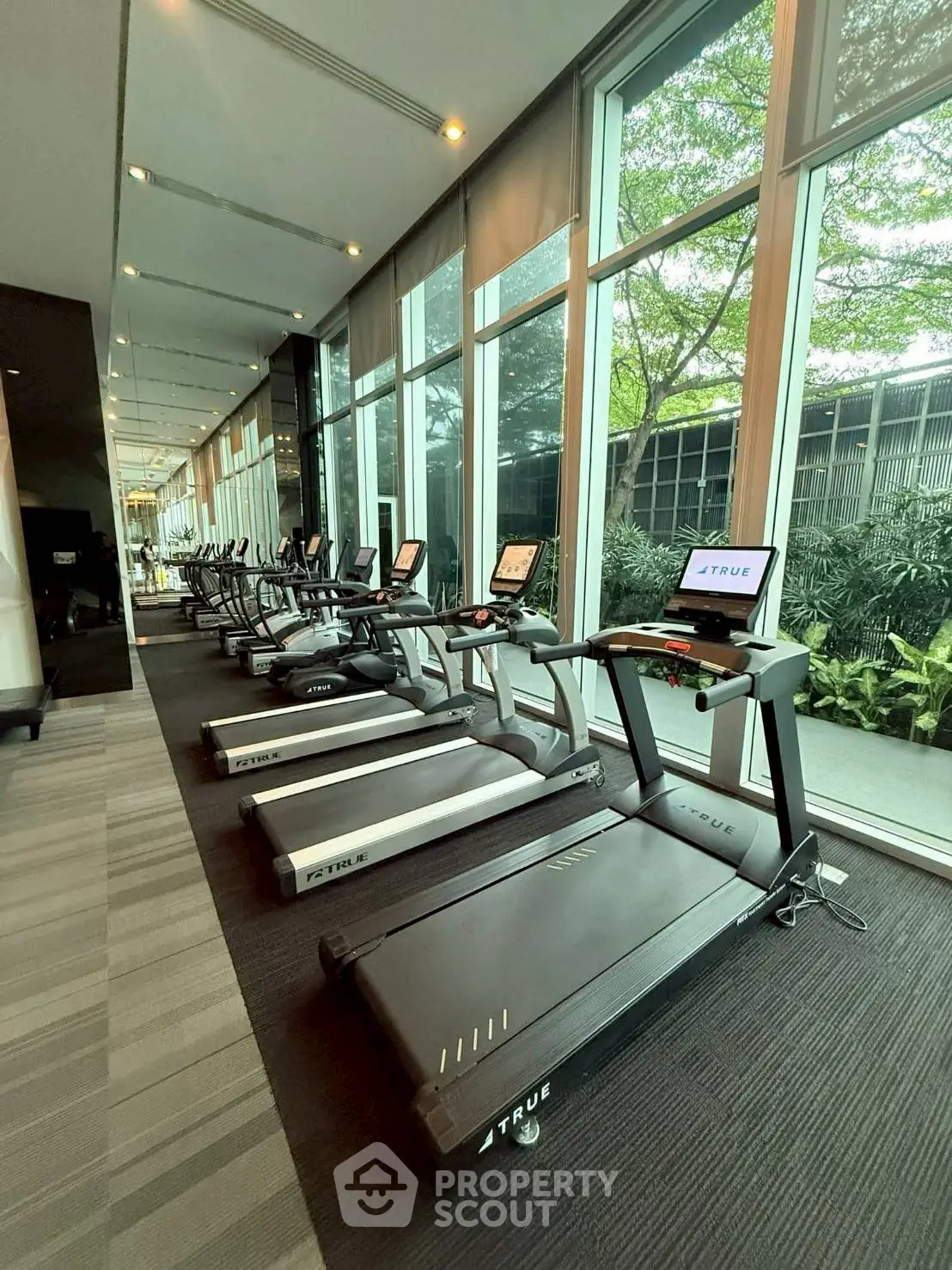 Modern gym with multiple treadmills and large windows overlooking greenery