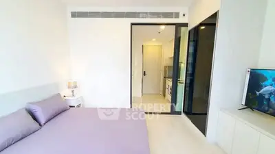 Modern bedroom with sleek design and open view to kitchen area, featuring a cozy bed and stylish decor.