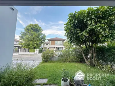 Charming suburban garden view with lush greenery and modern houses under a clear blue sky.