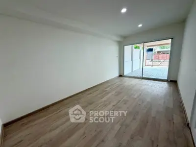 Spacious empty room with wooden flooring and large sliding glass doors leading to a patio.
