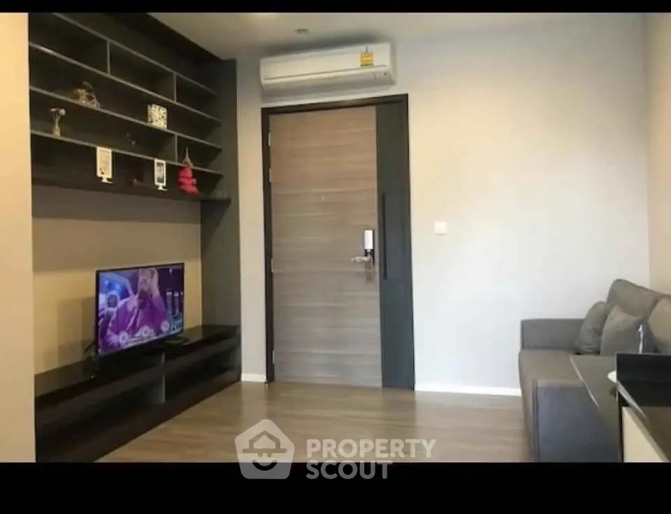 Modern living room with sleek shelving, TV, and cozy sofa, featuring a stylish wooden door and air conditioning.