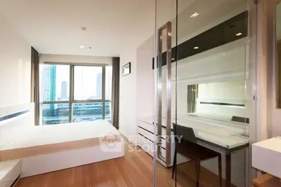 Modern bedroom with glass partition and city view, featuring sleek furniture and natural light.