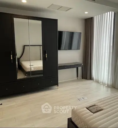 Modern bedroom with sleek black wardrobe and wall-mounted TV, featuring elegant floor-to-ceiling curtains.