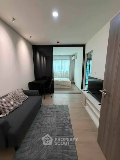 Modern apartment interior with cozy living room and stylish bedroom separated by glass doors.