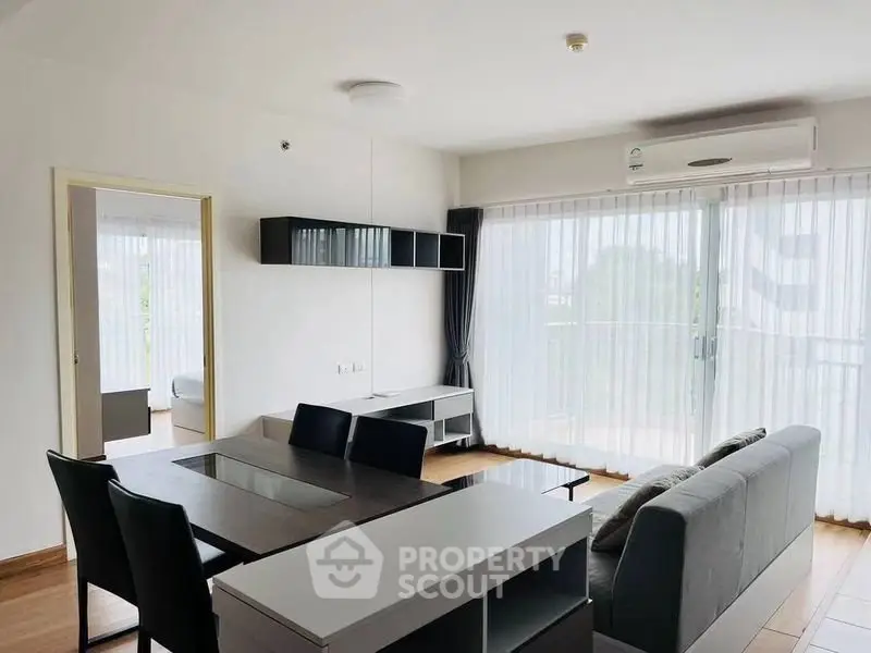 Modern living room with sleek furniture and large windows offering natural light and balcony access.