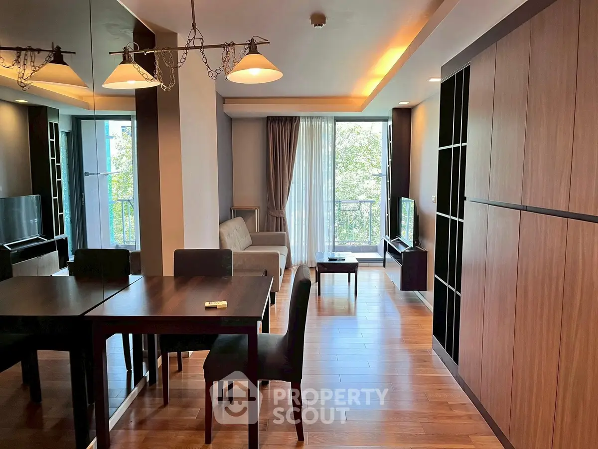 Modern living room with wooden flooring and elegant dining area, featuring large windows and stylish lighting.