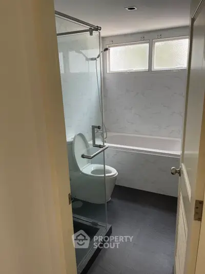 Modern bathroom with glass shower and bathtub, featuring sleek design and natural light.