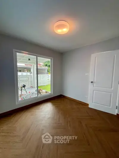 Bright empty room with wooden flooring and large window overlooking garden