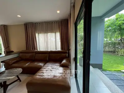 Spacious living room with leather sofa and garden view through sliding glass doors.