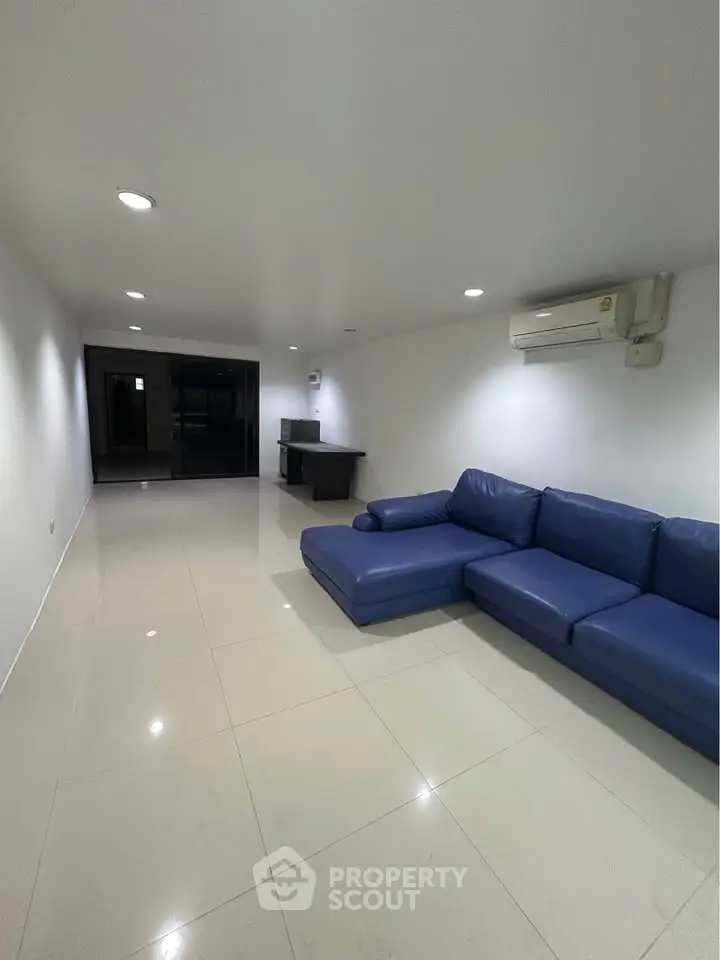 Spacious living room with modern blue sofa and sleek tiled flooring, perfect for relaxation and entertainment.
