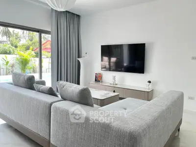 Modern living room with sleek gray sofa, wall-mounted TV, and large window overlooking lush greenery.