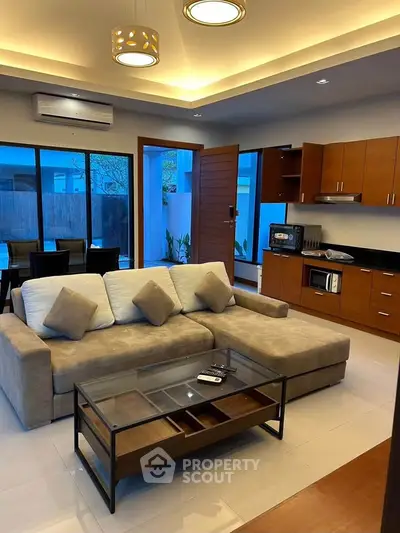 Modern living room with open kitchen, featuring stylish furniture and ambient lighting.