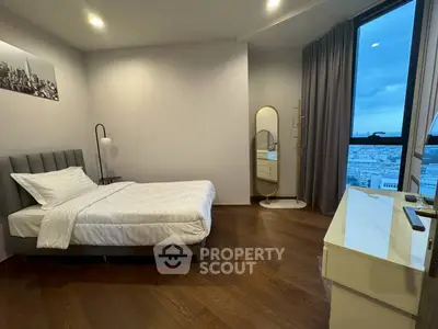 Modern bedroom with city view, featuring sleek furniture and wooden flooring.